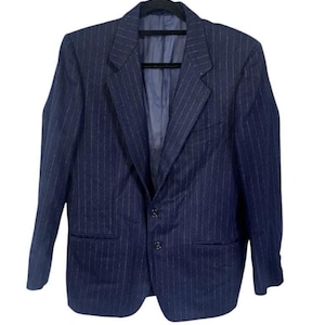 May include: Navy blue blazer with a pinstripe design. The blazer has a two-button closure, a notched lapel, and two front pockets. The jacket is hanging on a black hanger against a white background.