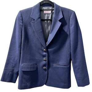 May include: A navy blue blazer with a classic design, featuring a notched lapel, three gold-coloured buttons, and two front pockets. The blazer is hanging on a black hanger against a white background.