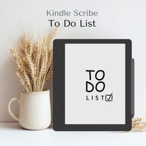 Könnte beinhalten: Ein schwarzer Kindle Scribe E-Reader mit einem weißen Bildschirm, auf dem eine handgeschriebene "TO DO LIST" mit einem Häkchen angezeigt wird. Der E-Reader befindet sich auf einer weißen Oberfläche mit einer beigefarbenen Tasse und Weizenähren im Hintergrund.