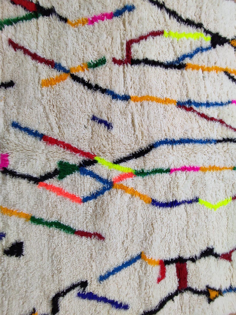 K&ouml;nnte beinhalten: Cremefarbener, strukturierter Teppich mit einem lebendigen, abstrakten Design. Der Teppich weist farbenfrohe, unregelm&auml;&szlig;ige Linien in Rot-, Blau-, Gelb-, Gr&uuml;n-, Rosa- und Schwarzt&ouml;nen auf. Die Linien sind &uuml;ber die Oberfl&auml;che verstreut und erzeugen einen modernen, k&uuml;nstlerischen Look.
