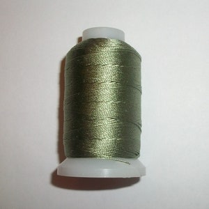 May include: A spool of olive green thread, tightly wound around a white plastic base. The thread has a subtle sheen, suggesting a silk or satin material. Ideal for sewing, embroidery, or other craft projects.
