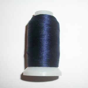 May include: A spool of navy blue thread. The thread is tightly wound around a white plastic spool. The thread has a slight sheen, suggesting a smooth texture. Ideal for sewing, embroidery, or other textile crafts.