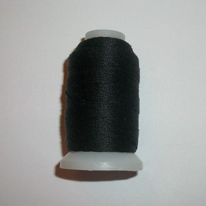 May include: A spool of black thread, tightly wound around a white plastic base. The thread appears to be a smooth, shiny material, suitable for sewing or crafting projects. The spool is centered against a plain white background.