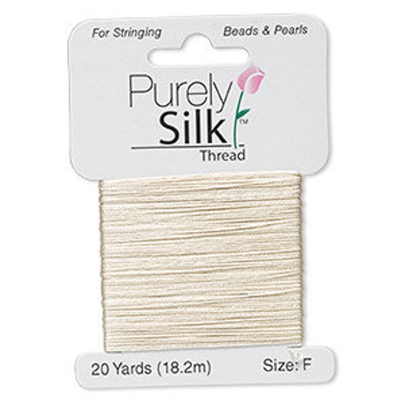 Op de afbeelding: Een spoel cr&egrave;mekleurig Purely Silk-garen, 18,2 meter, voor het rijgen van kralen. De draad zit op een witte kaart met de merknaam en een bloemenmotief. Maat F.