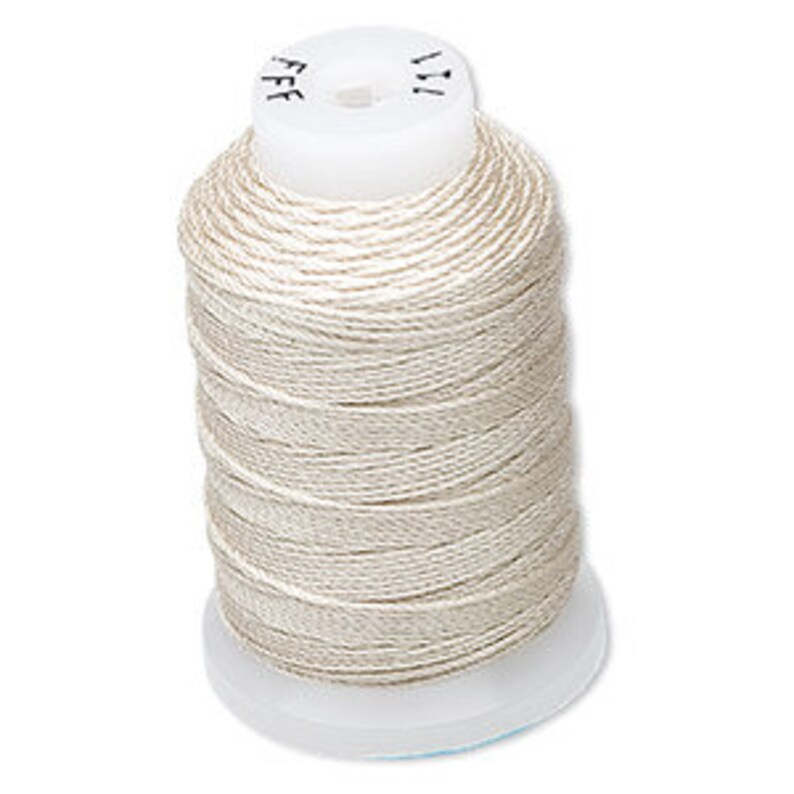 Op de afbeelding: Een spoel cr&egrave;mekleurig garen. De draad is strak gewikkeld rond een witte plastic spoel. De bovenkant van de spoel heeft kleine markeringen. De draad lijkt een lichte, neutrale kleur te hebben, geschikt voor diverse naaiprojecten.