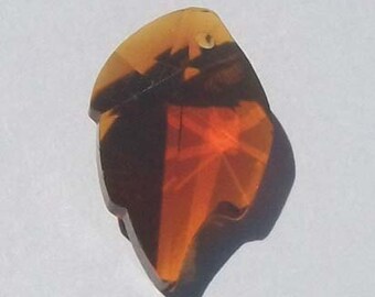 May include: A translucent, amber-colored pendant with a bird-like shape. The pendant has a dark brown interior with a small hole near the top. The design features a mix of light and dark amber hues, creating a striking visual effect.
