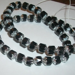 Op de afbeelding: Strengen zwarte facetkralen met zilverkleurige metalen accenten. De kralen zijn aan elkaar geregen, waardoor een flexibele ketting ontstaat. De kralen hebben een geometrische vorm en een glanzende afwerking.