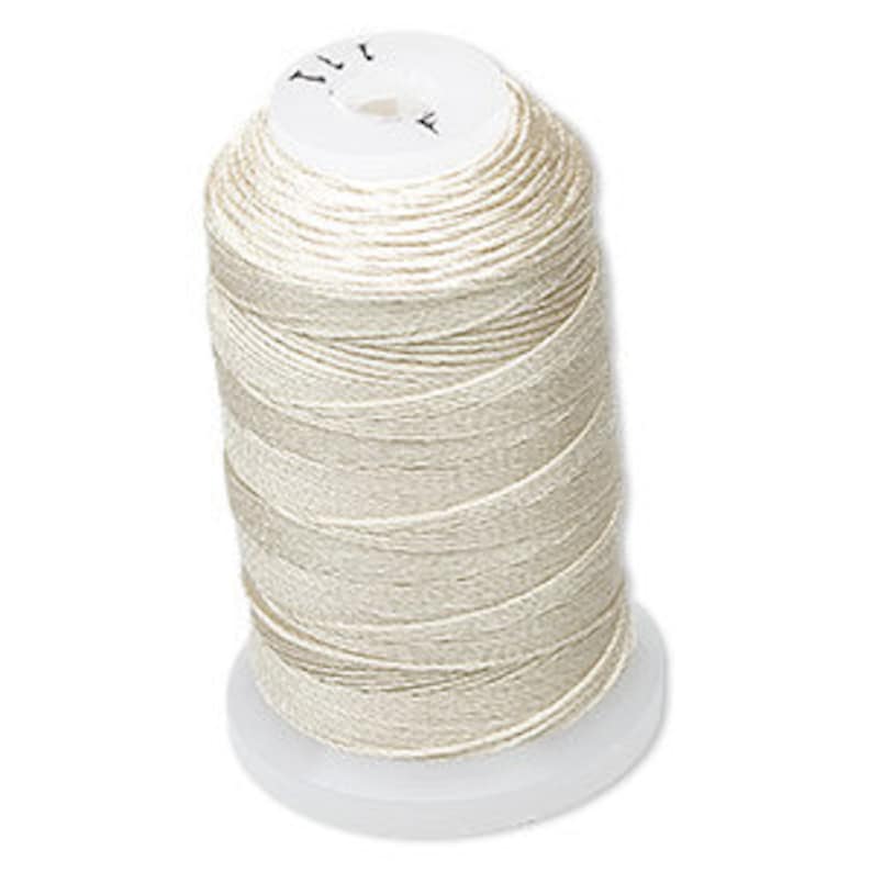 Op de afbeelding: Een spoel cr&egrave;mekleurig garen. De draad is strak gewikkeld rond een witte plastic spoel. De bovenkant van de spoel heeft een cirkelvormig ontwerp met tekst. De draad lijkt een fijn, glad materiaal te zijn.