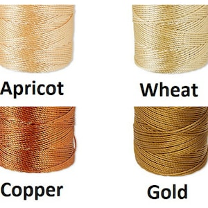 Peut inclure: Quatre bobines de cordon de couleurs abricot, bl&eacute;, cuivre et or. Chaque bobine est bien enroul&eacute;e, montrant la texture du mat&eacute;riau. Les couleurs sont &eacute;tiquet&eacute;es avec leurs noms respectifs en gras noir.