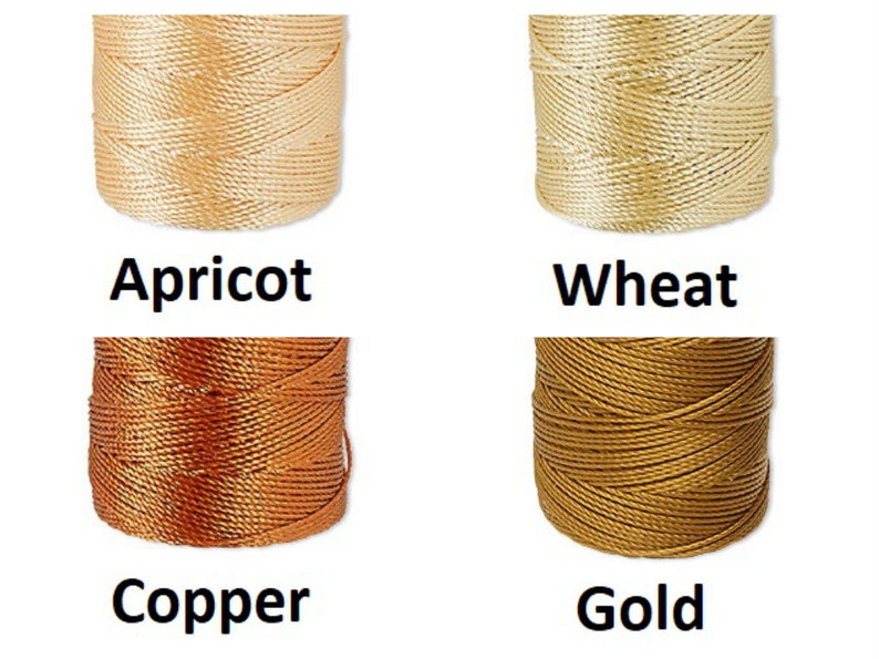 Peut inclure: Quatre bobines de cordon de couleurs abricot, bl&eacute;, cuivre et or. Chaque bobine est bien enroul&eacute;e, montrant la texture du mat&eacute;riau. Les couleurs sont &eacute;tiquet&eacute;es avec leurs noms respectifs en gras noir.