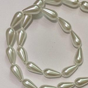 May include: Strand of pearlescent white teardrop-shaped beads. The beads are strung together, creating a flowing, elegant design. The beads have a smooth, glossy finish, reflecting light. Ideal for jewelry making or craft projects.