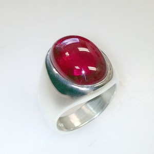 May include: A silver ring with a large, oval-shaped, red gemstone.