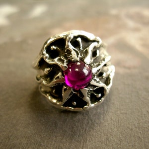 May include: A silver ring with a detailed design featuring a large, round, pink gemstone in the center.
