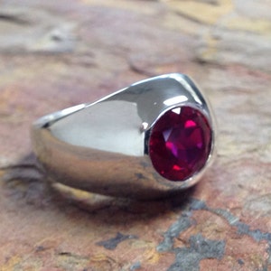 May include: A silver ring with a large, round, deep red gemstone.