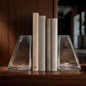 May include: Two clear, textured glass bookends with a trapezoidal shape flanking a row of four hardcover books. The books are titled Arranging Things, The Intangible, Axel Vervoordt Wabi Inspirations, and Remote Places to Stay, all in neutral tones.