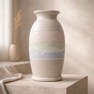 May include: A beige ceramic vase with a pastel painted design. The vase features a textured band of pink, green, and blue hues. The vase is cylindrical with a rounded base and a flared rim, suitable for home decor.