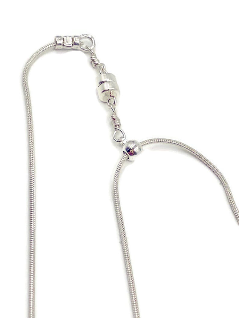 May include: A silver magnetic necklace with a snake chain style. The necklace has a magnetic clasp and a small silver bead.