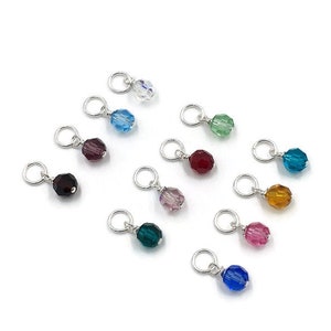 May include: Assortment of 12 small crystal beads in various colours, including clear, blue, green, purple, red, and pink. Each bead is attached to a silver jump ring.