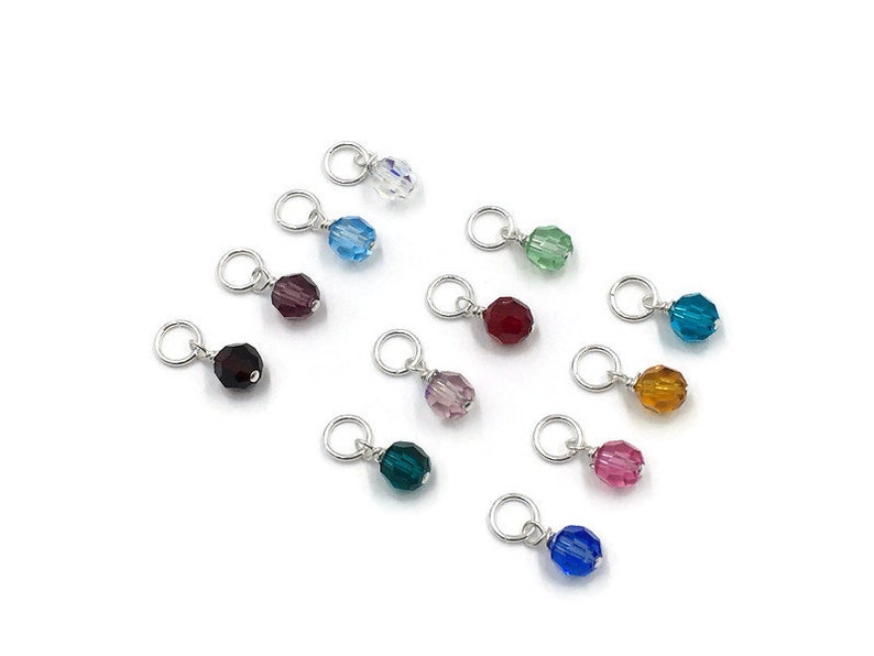 May include: Assortment of 12 small crystal beads in various colours, including clear, blue, green, purple, red, and pink. Each bead is attached to a silver jump ring.