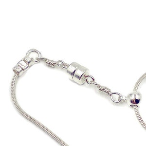 May include: A silver snake chain necklace with a magnetic clasp. The chain is made of small, round links and has a smooth, polished finish.