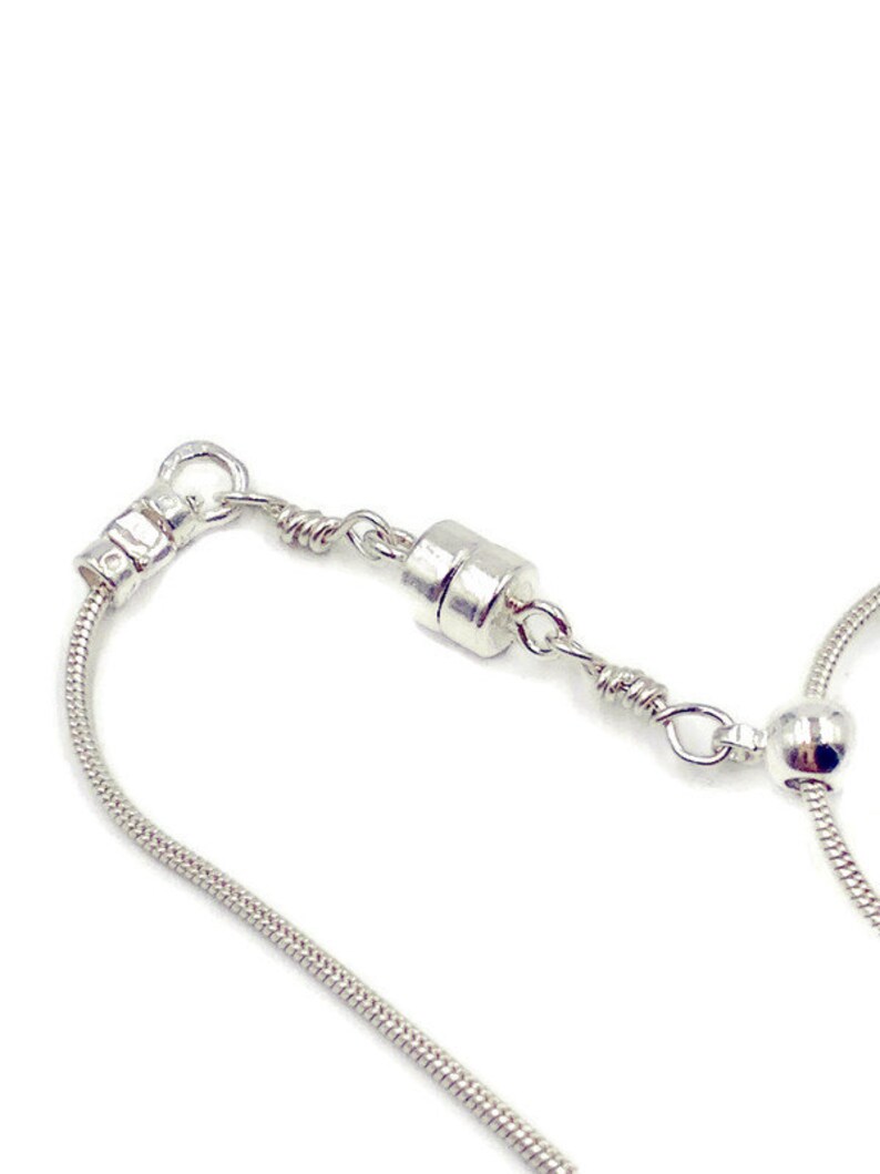 May include: A silver snake chain necklace with a magnetic clasp. The chain is made of small, round links and has a smooth, polished finish.