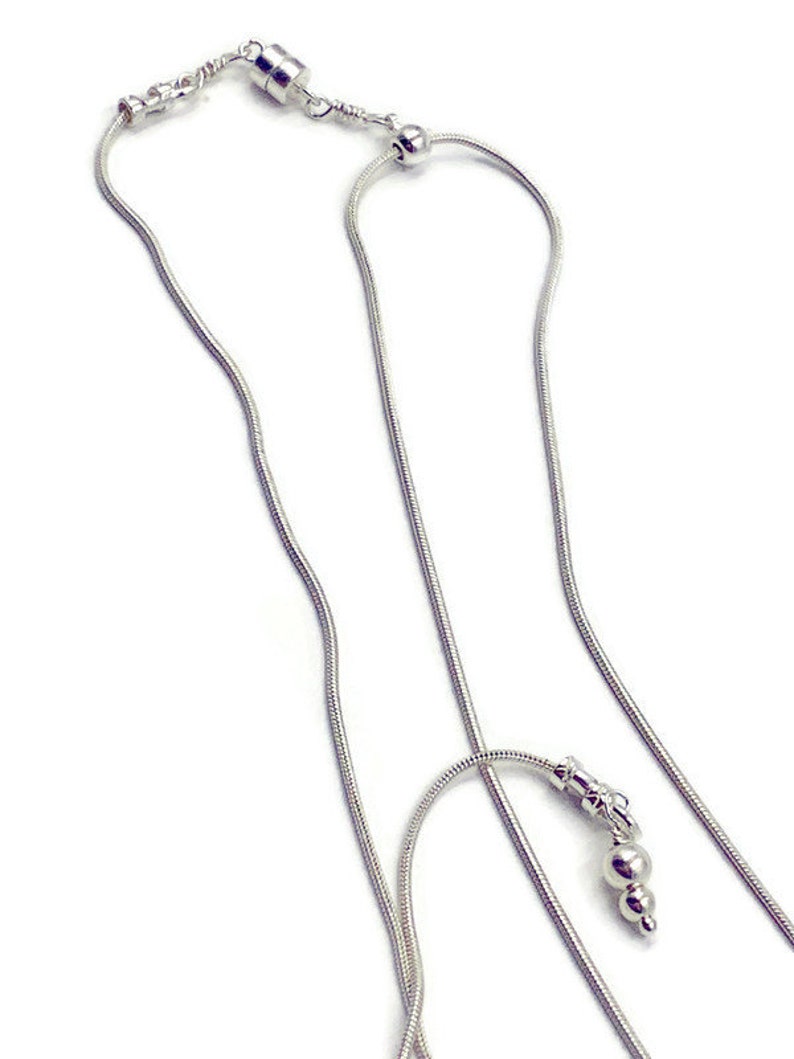 May include: A silver chain necklace with a magnetic clasp and a small silver bead at the end. The chain is made of a snake chain style.