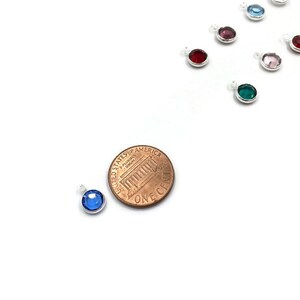 Pode incluir: Um close-up de um pingente de cristal azul, aproximadamente do tamanho de uma moeda de um centavo de euro. O pingente &eacute; feito de prata e apresenta um cristal azul redondo.