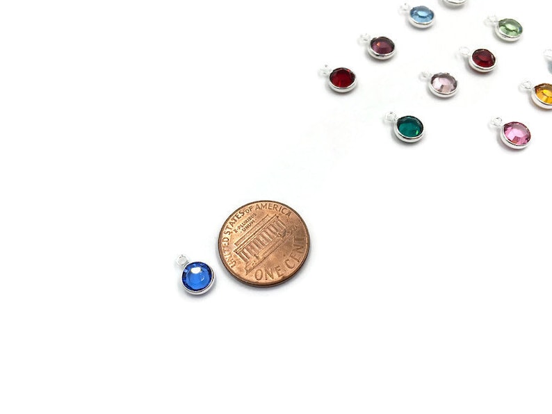 Pode incluir: Um close-up de um pingente de cristal azul, aproximadamente do tamanho de uma moeda de um centavo de euro. O pingente &eacute; feito de prata e apresenta um cristal azul redondo.