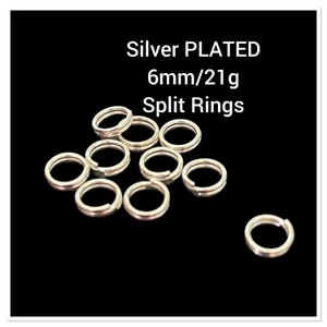 May include: Silver plated split rings, 6mm in diameter. The image shows a collection of small, shiny, silver-colored split rings, with the text "Silver PLATED 6mm/21g Split Rings" in white. The rings are arranged against a black background.