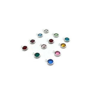 Pode incluir: Conjunto de pequenos pingentes redondos de prata com strass coloridos. Cada pingente apresenta um strass de cor diferente, incluindo vermelho, rosa, azul, verde e amarelo.