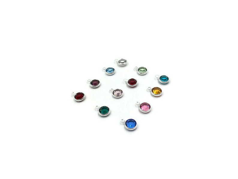 Pode incluir: Conjunto de pequenos pingentes redondos de prata com strass coloridos. Cada pingente apresenta um strass de cor diferente, incluindo vermelho, rosa, azul, verde e amarelo.