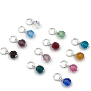 May include: Assortment of 12 crystal beads in various colours, each attached to a silver jump ring. The beads are faceted and have a shiny finish. The colours include clear, light blue, dark blue, red, purple, pink, green, teal, orange, and brown.
