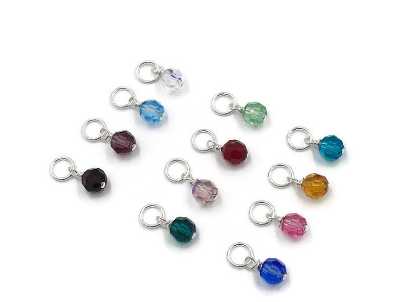 May include: Assortment of 12 crystal beads in various colours, each attached to a silver jump ring. The beads are faceted and have a shiny finish. The colours include clear, light blue, dark blue, red, purple, pink, green, teal, orange, and brown.