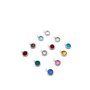 Pode incluir: Conjunto de 12 pequenos pingentes redondos com diferentes cores de pedras de cristal. Cada pingente tem um la&ccedil;o prateado para prender a uma pulseira ou colar.
