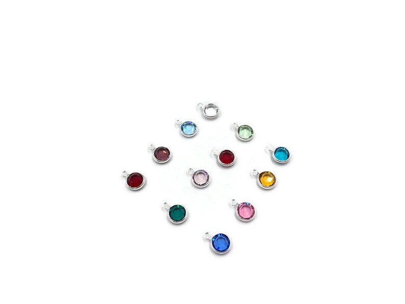 Pode incluir: Conjunto de 12 pequenos pingentes redondos com diferentes cores de pedras de cristal. Cada pingente tem um la&ccedil;o prateado para prender a uma pulseira ou colar.