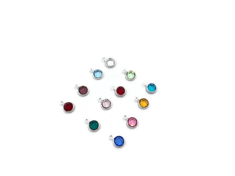 Pode incluir: Conjunto de 12 pequenos pingentes redondos com cristais de diferentes cores. Cada pingente tem um la&ccedil;o prateado para prender a um bracelete ou colar.