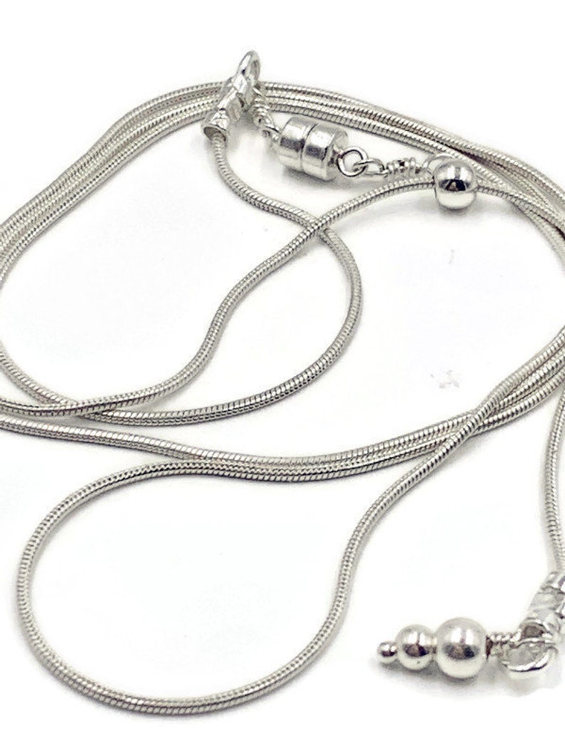 May include: A silver snake chain necklace with a magnetic clasp and a small silver bead accent.