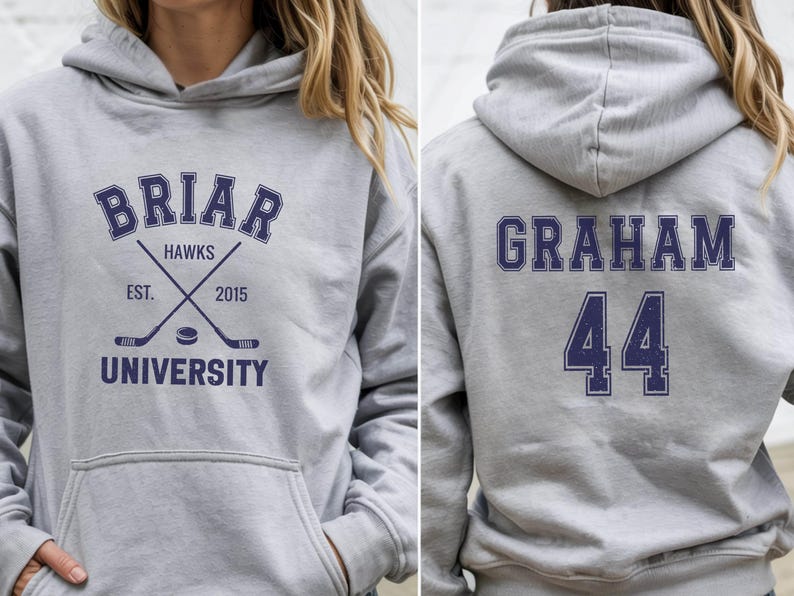 May include: A light gray hoodie with a front graphic that reads "Briar Hawks University" with crossed hockey sticks and a puck. The back of the hoodie displays the name "Graham" and the number "44" in navy blue.