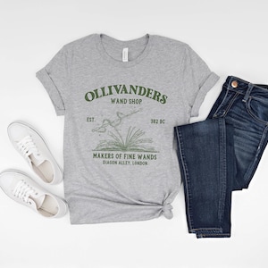 May include: A gray t-shirt with a green graphic of Ollivanders Wand Shop. The graphic includes the text "Ollivanders Wand Shop", "Est. 382 BC", and "Makers of Fine Wands Diagon Alley, London".