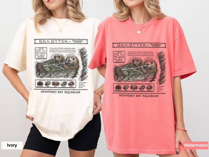 May include: Two short-sleeved t-shirts, one ivory and one watermelon, each featuring a detailed graphic of a sea otter with text that reads "Sea Otter - Enhydra Lutris" and "Monterey Bay Aquarium". The graphic includes illustrations of the otter and its food sources.
