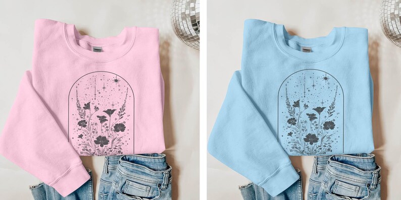 May include: Two sweatshirts with a floral design. One is pink and the other is light blue. Both have a black outline of a flower arrangement with a starry sky inside an arch.