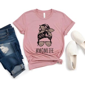 May include: A pink t-shirt with a graphic of a woman with a messy bun and sunglasses. The text "#MOMLIFE" is printed below the graphic.