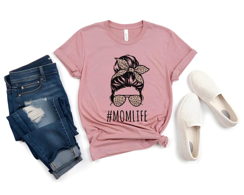 May include: A pink t-shirt with a graphic of a woman with a messy bun and sunglasses. The text "#MOMLIFE" is printed below the graphic.