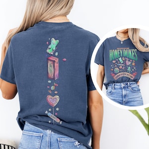 Może przedstawiać: Granatowa koszulka z kolorową grafiką cukierk&oacute;w i napisem "Honeydukes Legendary Wizarding Sweet Shop". Tył koszulki ma pionowy wz&oacute;r żelka, pudełka po cukierkach i lizak&oacute;w. Koszulka jest w wygodnym, swobodnym stylu.