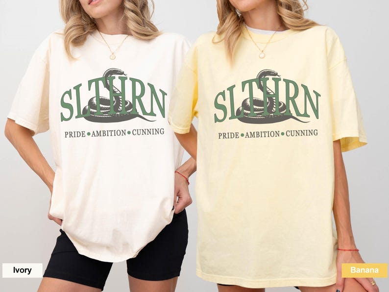 May include: Two t-shirts with a green snake graphic and the text "SLITHERN PRIDE AMBITION CUNNING". The shirt on the left is ivory and the shirt on the right is banana.