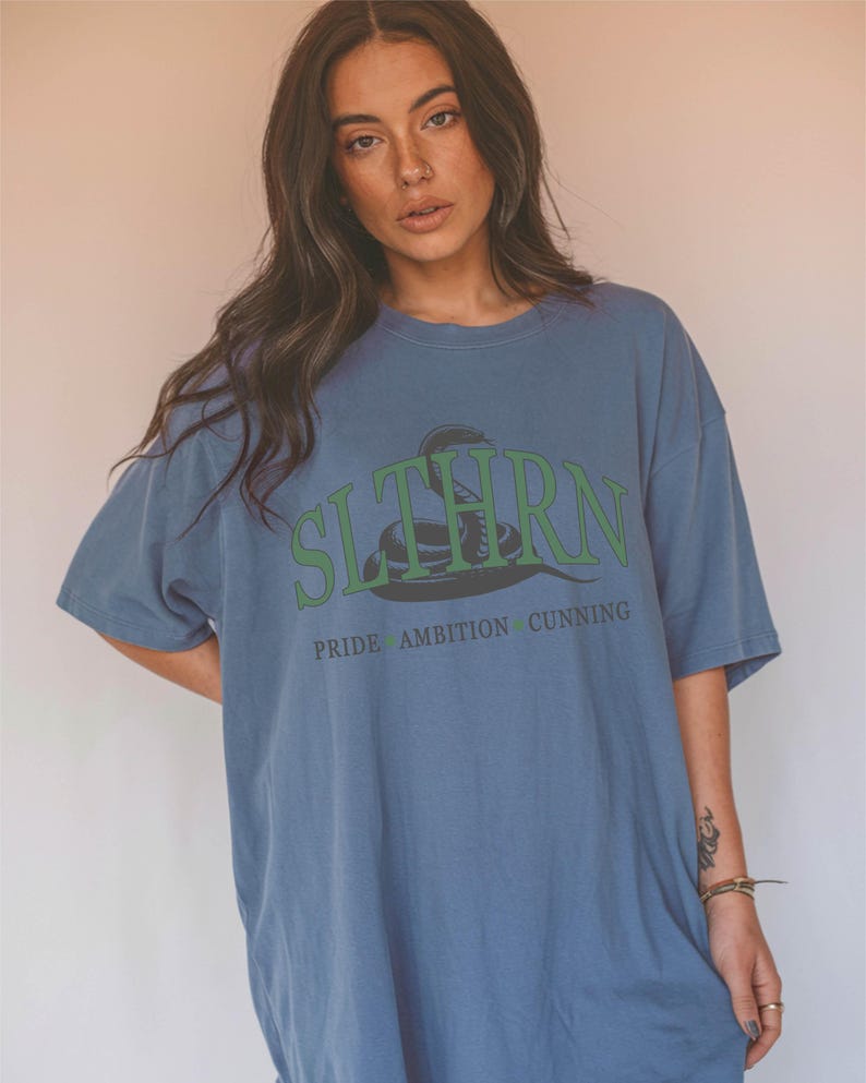 May include: A blue oversized t-shirt with a green snake graphic and the text "SLYTHERN" in green letters. Below the snake, the text "PRIDE AMBITION CUNNING" is printed in black.