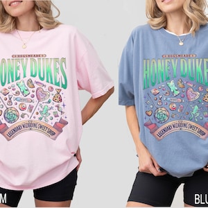 Może przedstawiać: Dwie duże koszulki, jedna r&oacute;żowa i jedna niebieska, każda z kolorową grafiką. Grafika zawiera tekst "HONEY DUKES" i "LEGENDARY WIZARDING SWEET SHOP" z ilustracjami cukierk&oacute;w. Koszulki są noszone z czarnymi szortami.