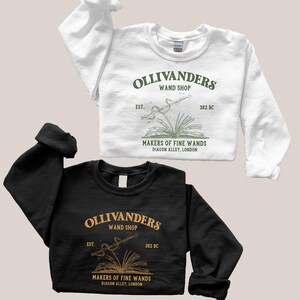 May include: Two black and white sweatshirts with a green graphic design of a wand and book. The text on the graphic reads "Ollivanders Wand Shop Est. 382 BC Makers of Fine Wands Diagon Alley, London."