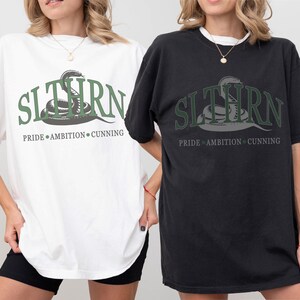 May include: Two oversized t-shirts with a snake graphic and the text "SLYTHERN PRIDE AMBITION CUNNING". One shirt is white and the other is black.
