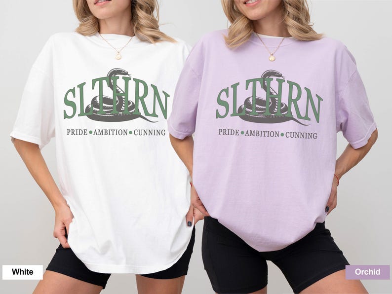 May include: Two t-shirts with a green snake graphic and the text "SLITHERN PRIDE AMBITION CUNNING". The shirt on the left is white and the shirt on the right is orchid.